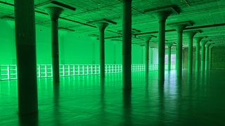 Ein grün erleuchteter, großer Raum mit vielen Säulen, die in Reihen stehen.
