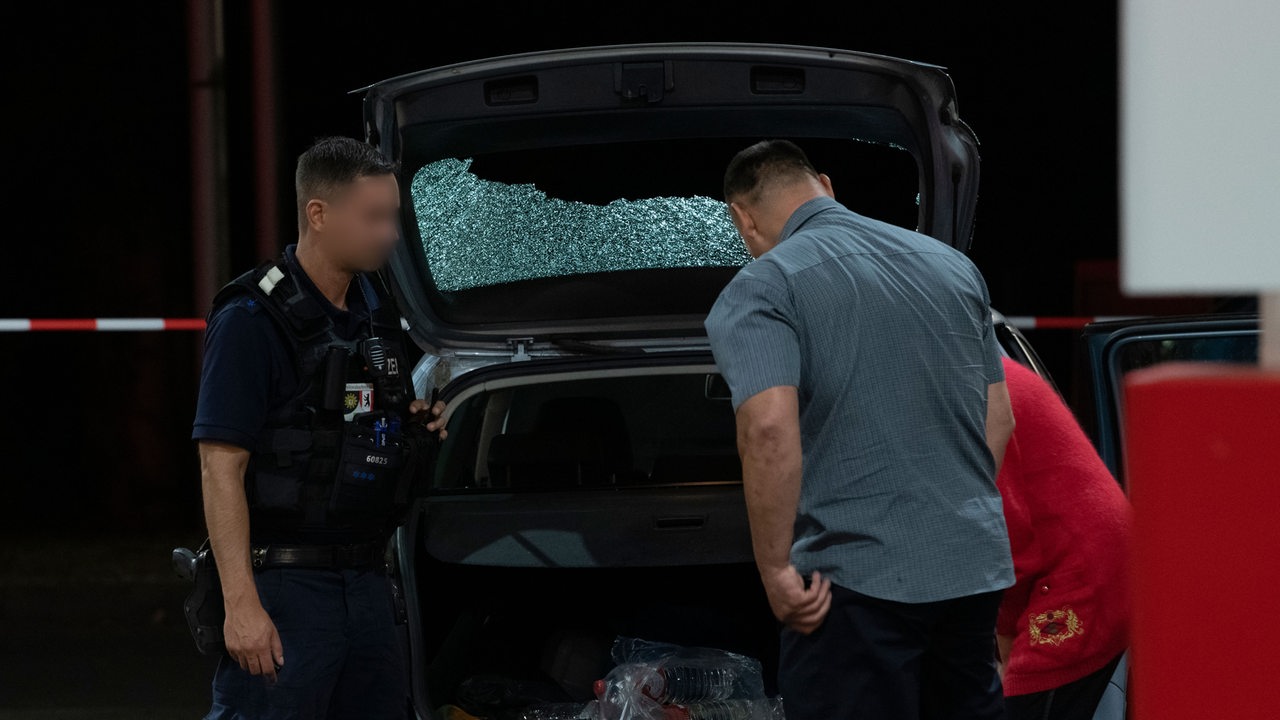 Zwei Personen und ein Polizist begutachten eine zersplitterte Auto-Heckscheibe