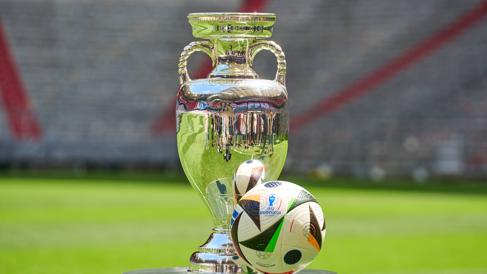 EM-Pokal und EM-Ball auf einem Tisch vor Stadionkulisse