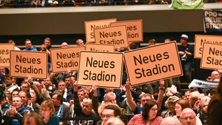 Gäste halten Schilder mit der Aufschrift "Neues Stadion" hoch 