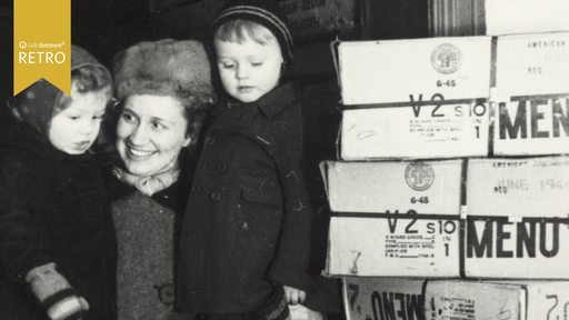 Historisches Foto zeigt eine Mutter mit zwei Kindern, die sich über die Ankunft der Care-Pakete freut.