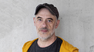 Der Schriftsteller Stephan Lohse steht vor einer grauen Wand und schaut in die Kamera