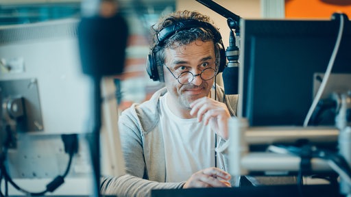 Mann mit Kopfhörer vor dem Mikrofon im Sendestudio