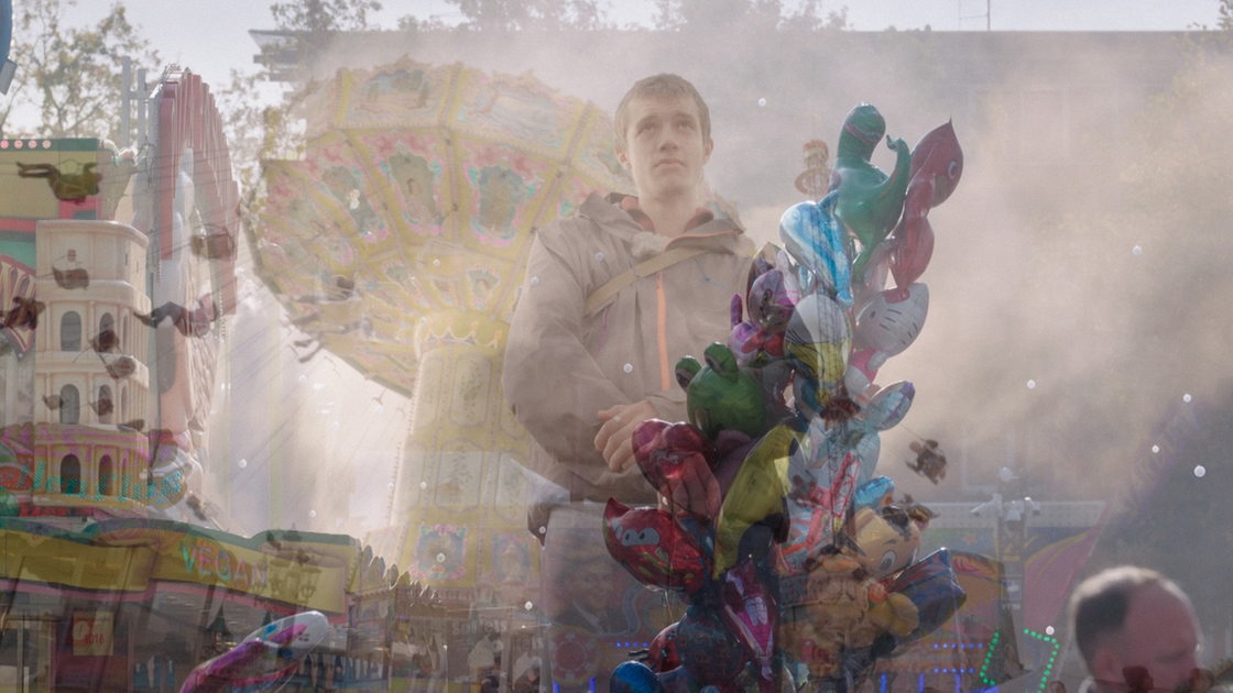 Keyvisual zum Thema Autismus: Hinter Nebel sieht man einen jungen Mann auf einem Jahrmarkt