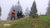 Wandergruppe auf einem Hügel vor einem Tannenwald