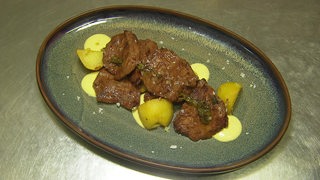 Das peruanische Gericht Anticucho ist auf einem Teller angerichtet. Kartoffeln, darauf liegt Rinderroastbeef.