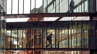 Zwei Menschen laufen über einen gläsernen Übergang zwischen zwei Gebäuden