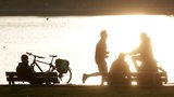 Menschen auf Fahrrädern und Parkbänken im Gegenlicht.