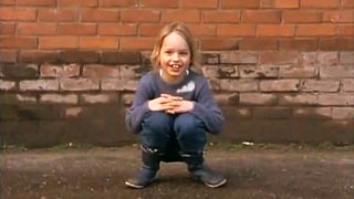 Ein Mädchen sitzt in der Hocke und lacht.