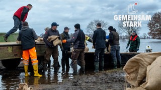 Lilienthal: Landwirte transportieren Sandsäcke per Boot zum durchweichten Deich. Logo: Gemeinsam stark!