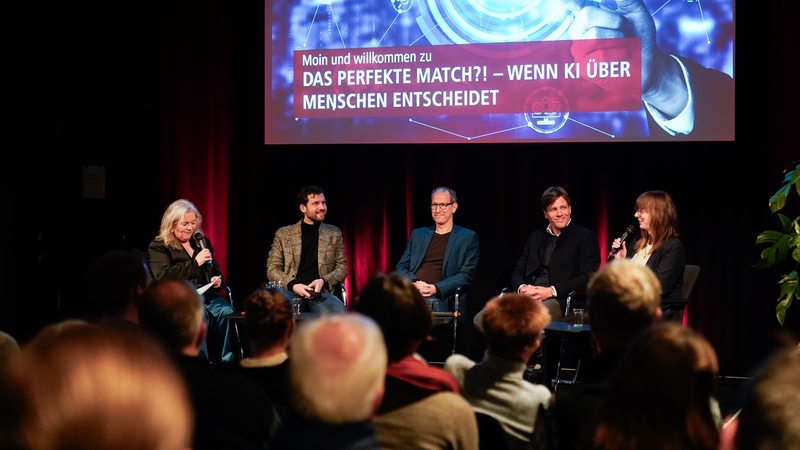 Zwei Frauen und drei Männer bei einer Podiumsdiskussion vor Publikum