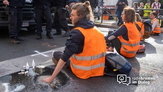 Klimaaktivisten mit orangen Warnwesten haben sich mit den Händen auf einer Straße festgeklebt