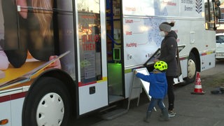 Eine Frau und ein Kind stehen vor der Seitentür eines Busses.