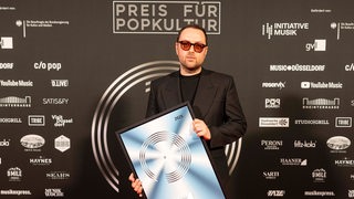 Kim Frank hält seine Auszeichnung vom Preis für Popkultur in der Hand.