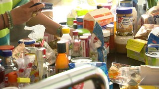 Eine Person sortiert viele verschiedene Lebensmittel, die auf einer Küchenplatte stehen.