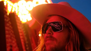 Der Schauspieler Lasse Sehsted Skafte als Cowboy mit dem Liberace Schriftzug spiegelnd in der Sonnenbrille. 