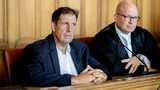 Ein Mann sitzt auf der Anklagebank eines Gerichts. Neben ihm sein Anwalt. 