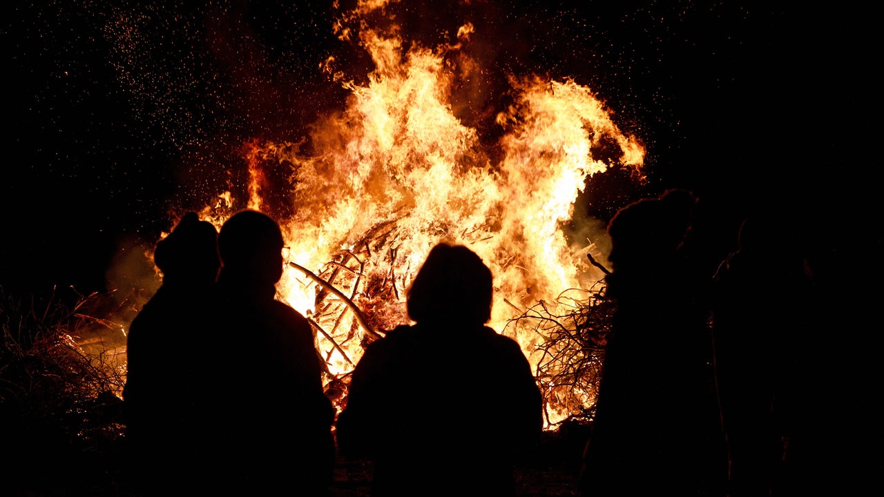 Silhouetten von Menschen vor einem brennenden Osterfeuer (Symbobild)