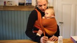 Eine junge Mutter mit ihrem Baby im Tragetuch trägt sich in eine Liste ein