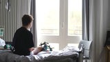 Ein junger Mann sitzt auf einem Krankenhausbett. An seinem operierten Bein ist ein großes Gestell befestigt