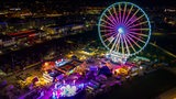 Ein Riesenrad steht im Dunkeln auf einem Jahrmarkt und ist bunt erleuchtet. 