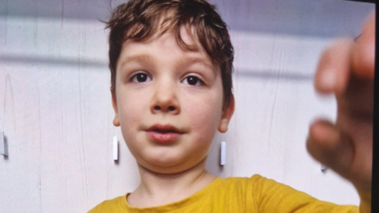 Ein kleiner Junge in gelbem Shirt schaut in eine Kamera