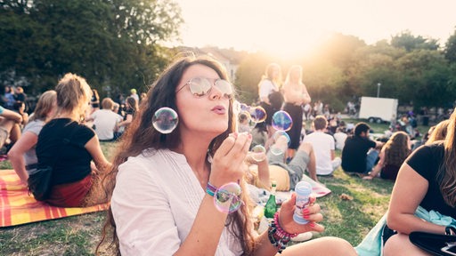 Summer Sounds, Frau bläst Seifenblasen sitzend auf der Wiese