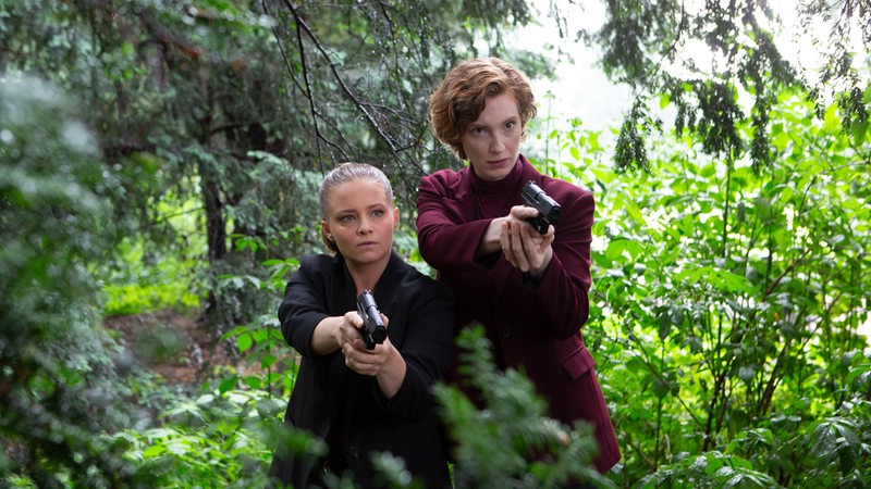 Liv Moormann (Jasna Fritzi Bauer) und Linda Selb (Luise Wolfram) stehen bewaffnet im Wald und blicken konzentriert nach vorne.