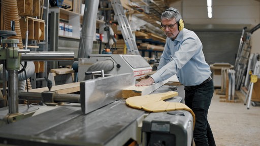Ein Mann arbeitet mit Ohrenschutz in einer Tischlerwerkstatt