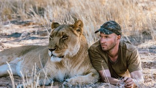 Valentin Grüner liegt mit einer Löwin in der Savanne