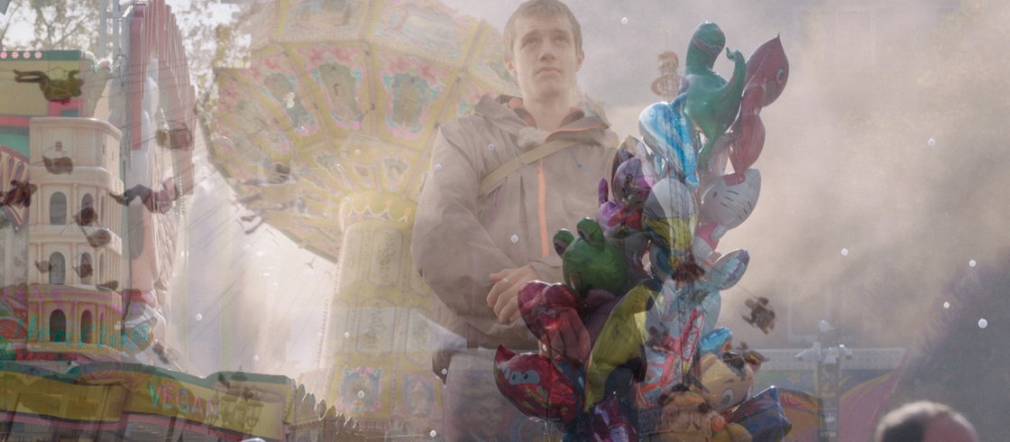 Keyvisual zum Thema Autismus: Hinter Nebel sieht man einen jungen Mann auf einem Jahrmarkt